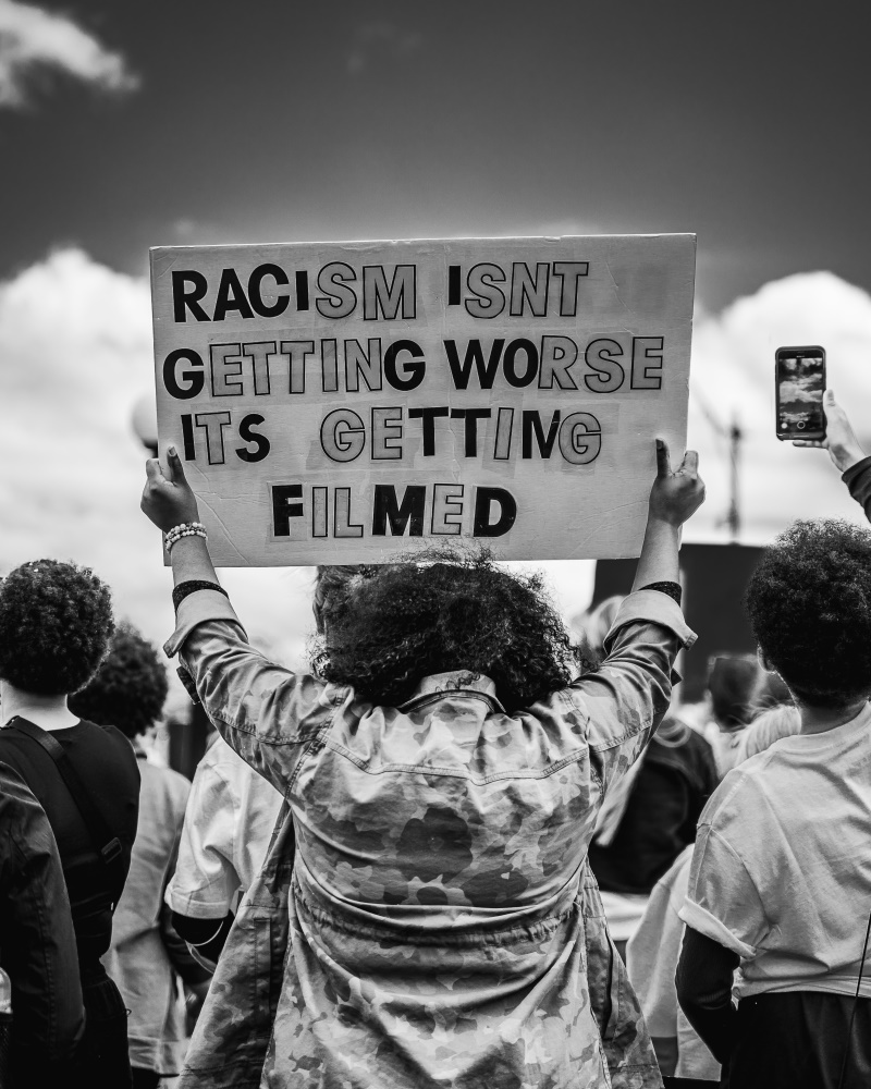 Protestor holding sign that says "Racism isn't getting worse, it's getting filmed"